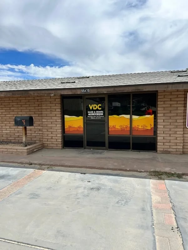 Brick storefront with VDC sign and sunset-themed window display under blue sky with clouds
